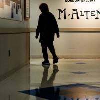 Silhouette walking in front of lit up wall that says "M. Alten"